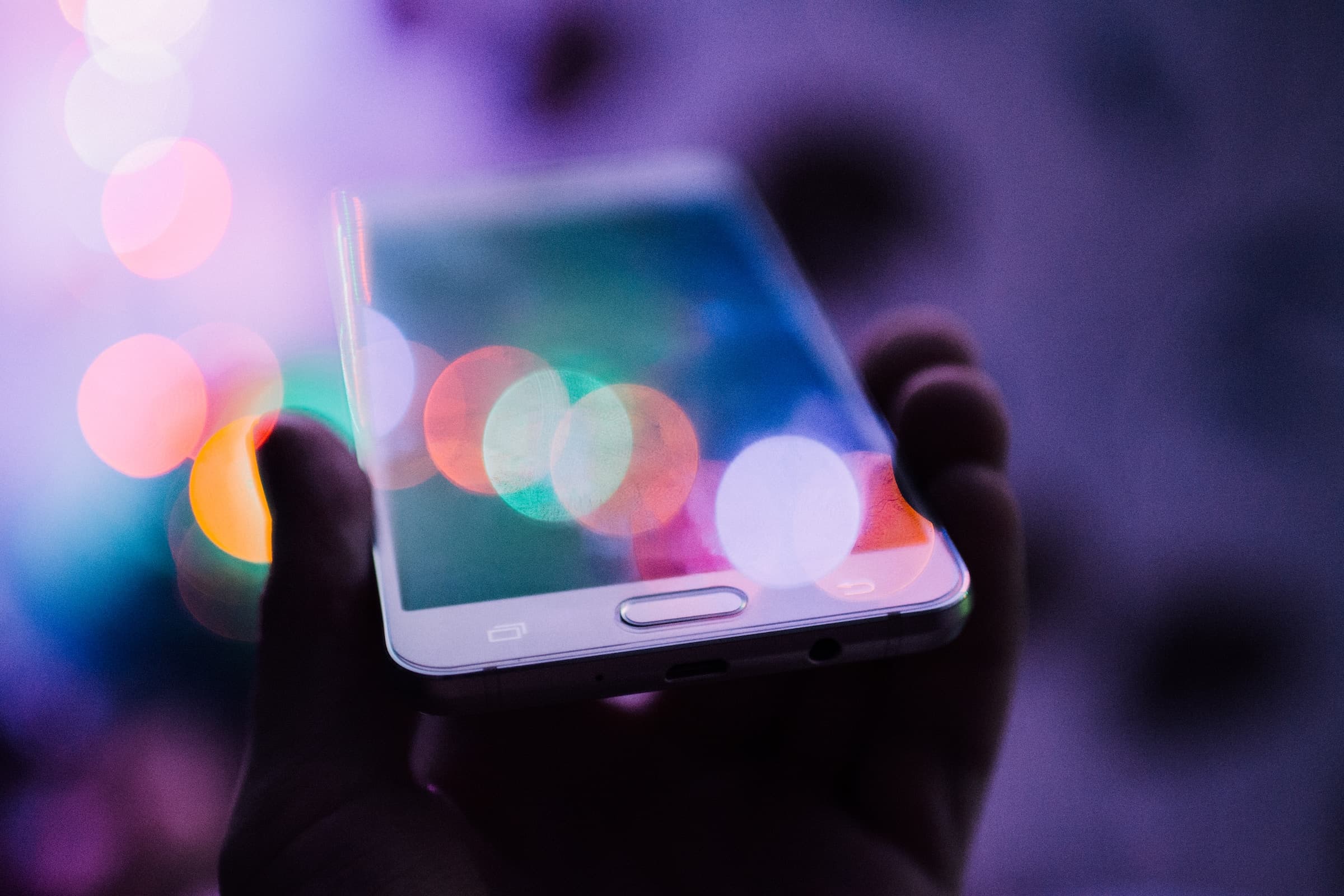 A person holding a smartphone with a colorful bokeh effect on the screen